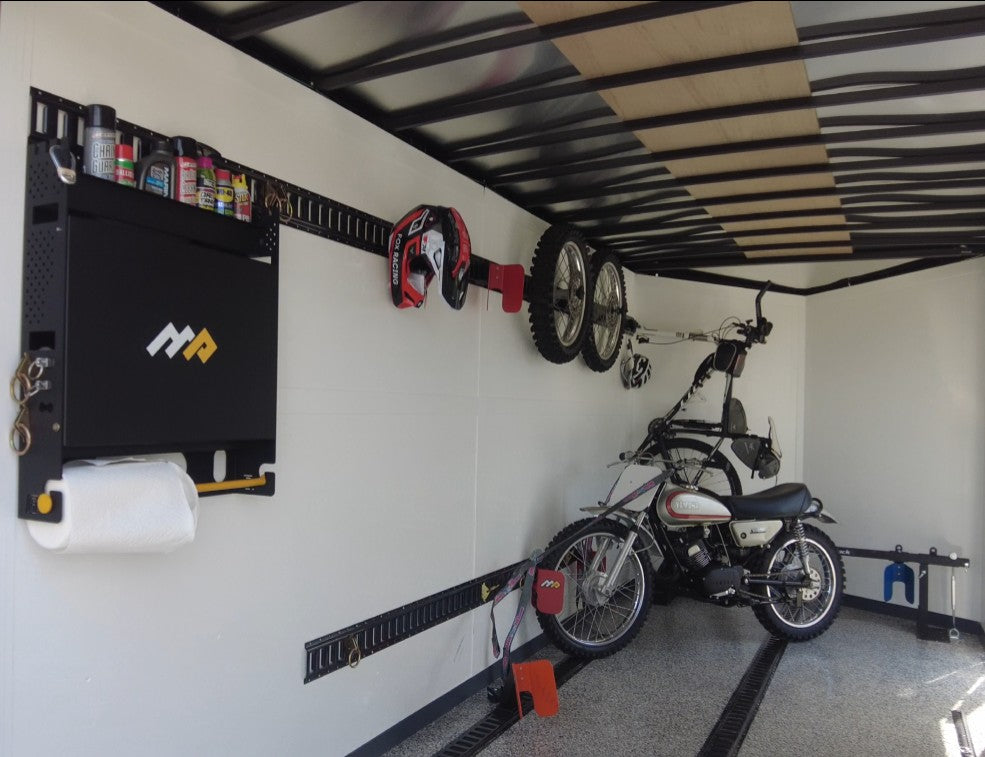 MotoProHQ Dirt Bike Trailer Wall Organizer with shelf closed mounted in dirt bike trailer. There are various lubricants and chemicals stored on the organizer shelf as well as storage for max or e-track tie down rings. Dirt bike secured using MotoProHQ EZ Chock system and straps.